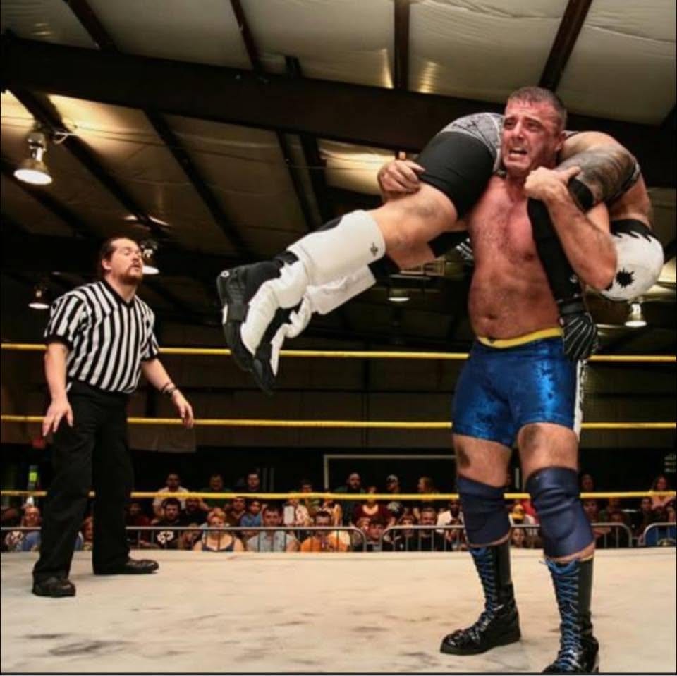 Duke Warfield lifting an opponent overhead as the referee watches